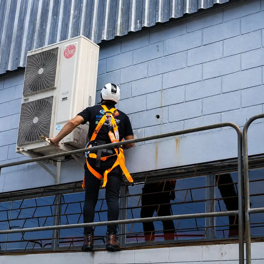 Técnico com cinto de segurança e capacete atendendo condensadora em altura